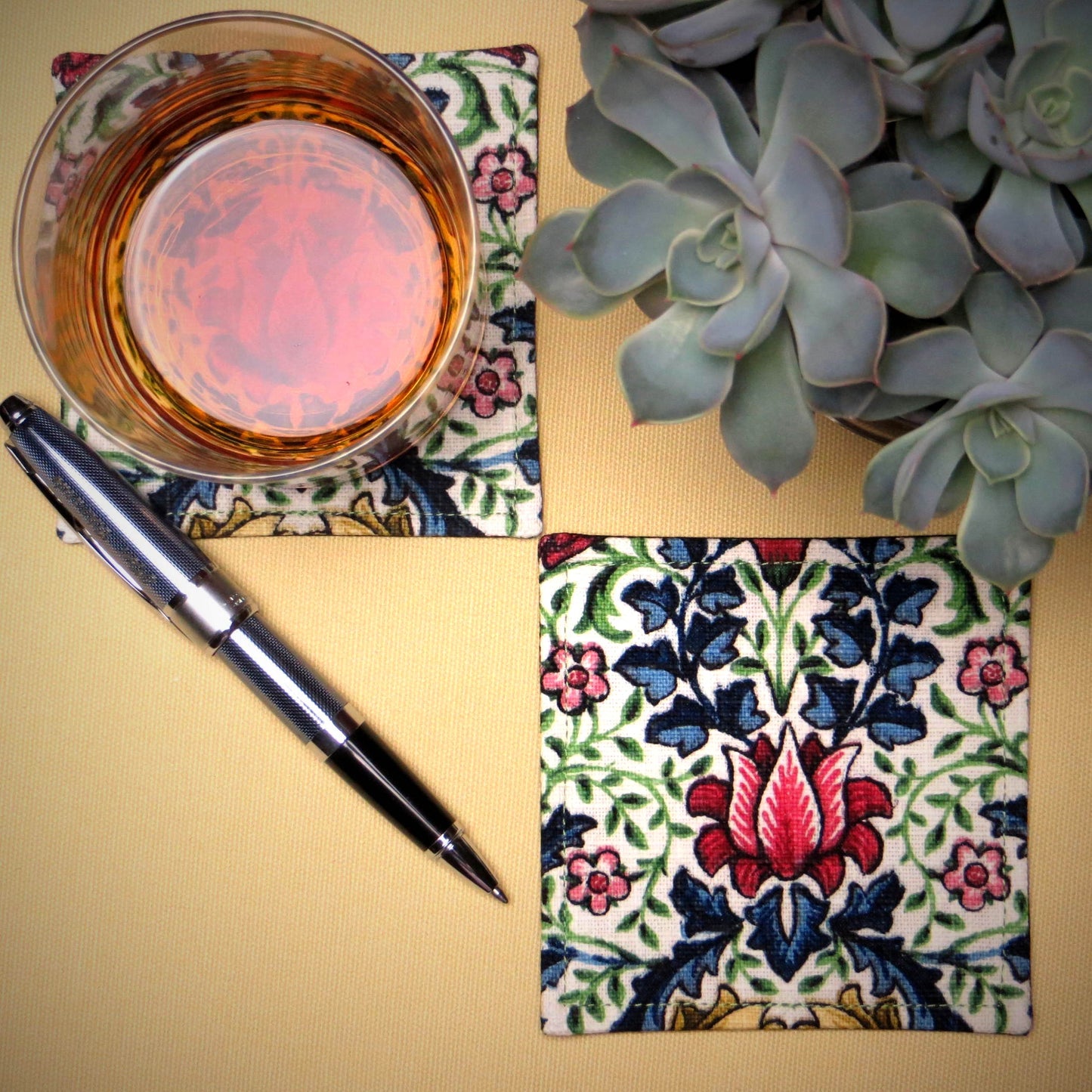 Square coasters with red, blue, green, and yellow flowers and leaves on off white background