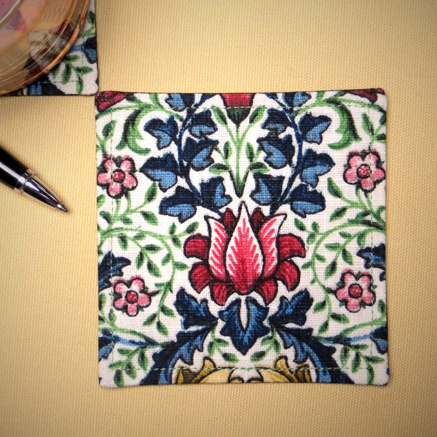 Square coasters with red, blue, green, and yellow flowers and leaves on off white background