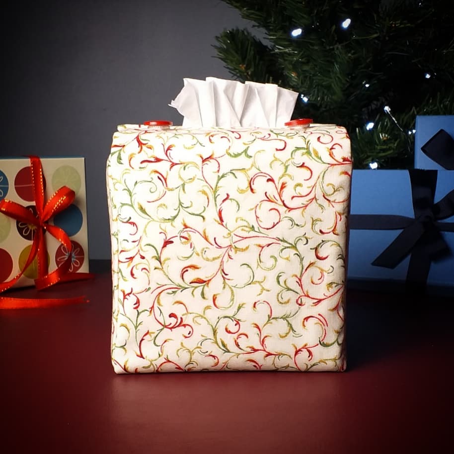 Square tissue box cover with holiday themed red and green swirls with metallic gold accent on cream colour background