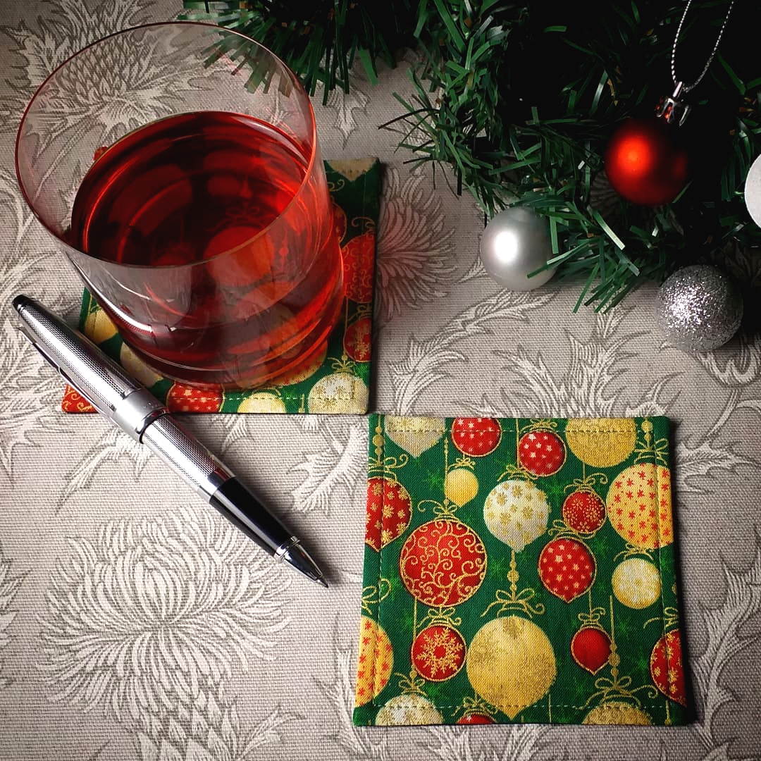 Square coasters with holiday themed red, gold, and white baubles on green background