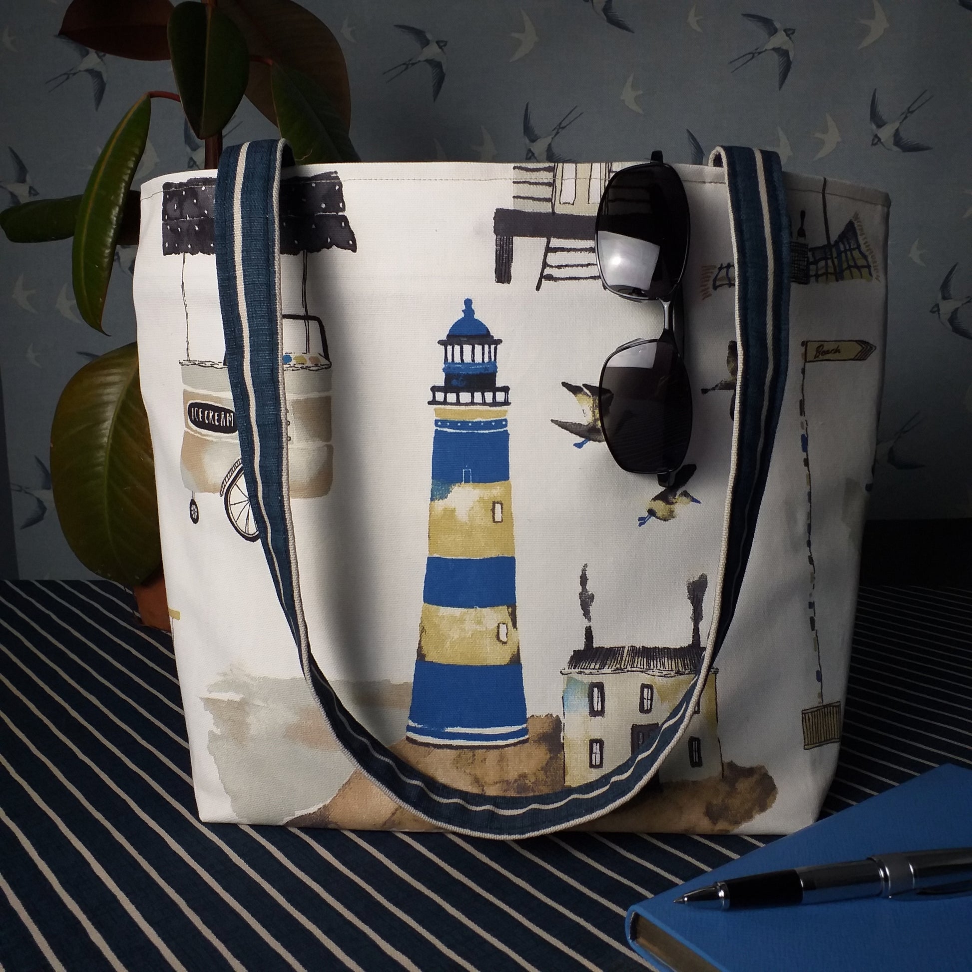 Large tote bag with multi-colour beach huts, lighthouse, seaside shops design on off-white background
