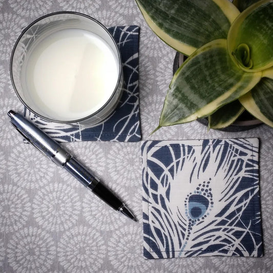 Square coasters with white peacock feathers design on blue background