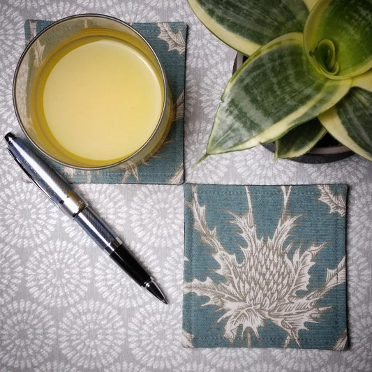 Square coasters with white thistle design on teal blue background
