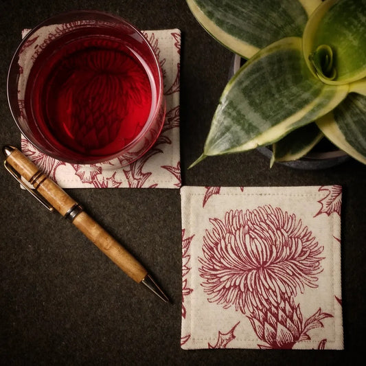 Square coasters with red thistle design on off-white background