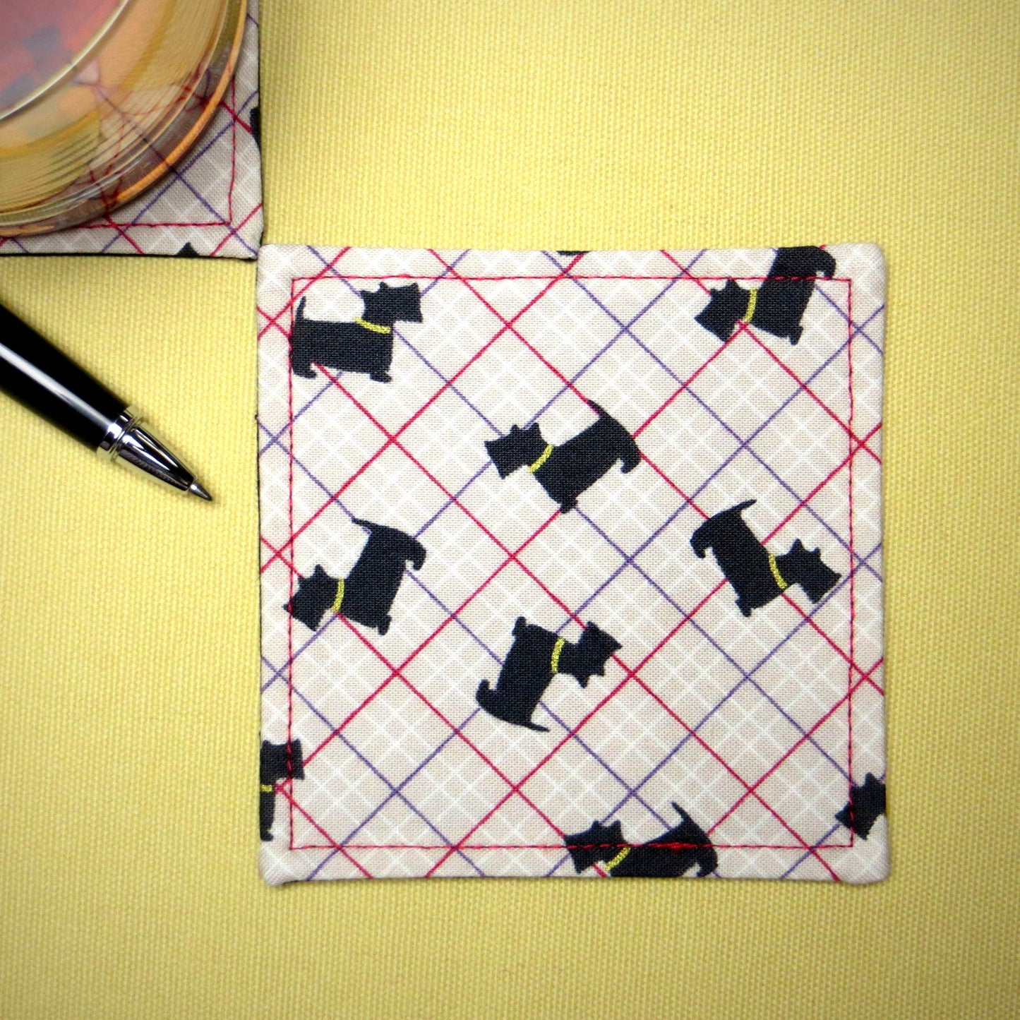 Square coasters with Scottish Terrier dogs design on beige background with red, purple, and white grid