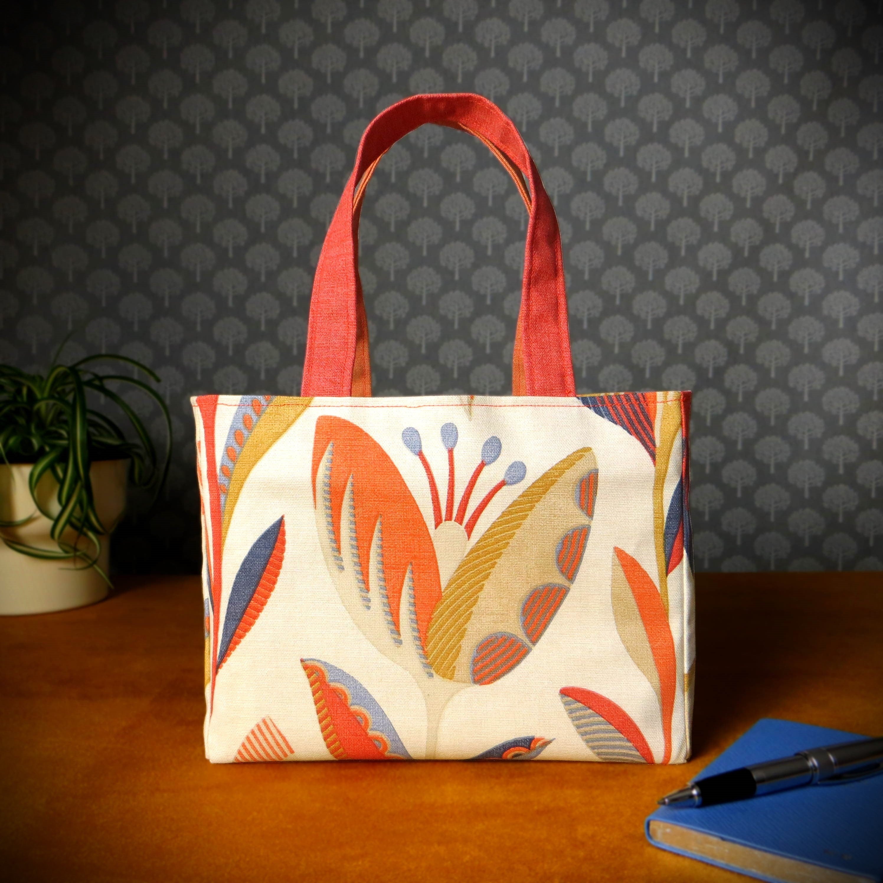 Small cotton tote bag with tulip pattern in shades of warm orange, rich ochre, and classic denim blue on an off-white background