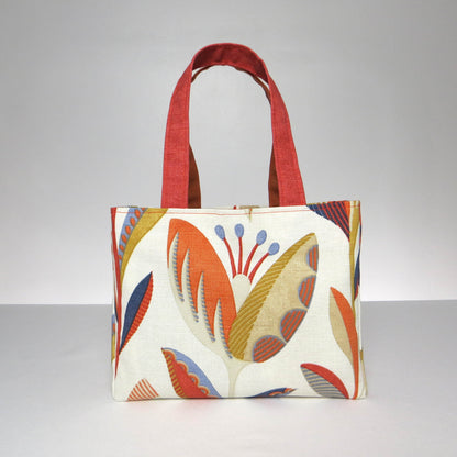 Small cotton tote bag with tulip pattern in shades of warm orange, rich ochre, and classic denim blue on an off-white background