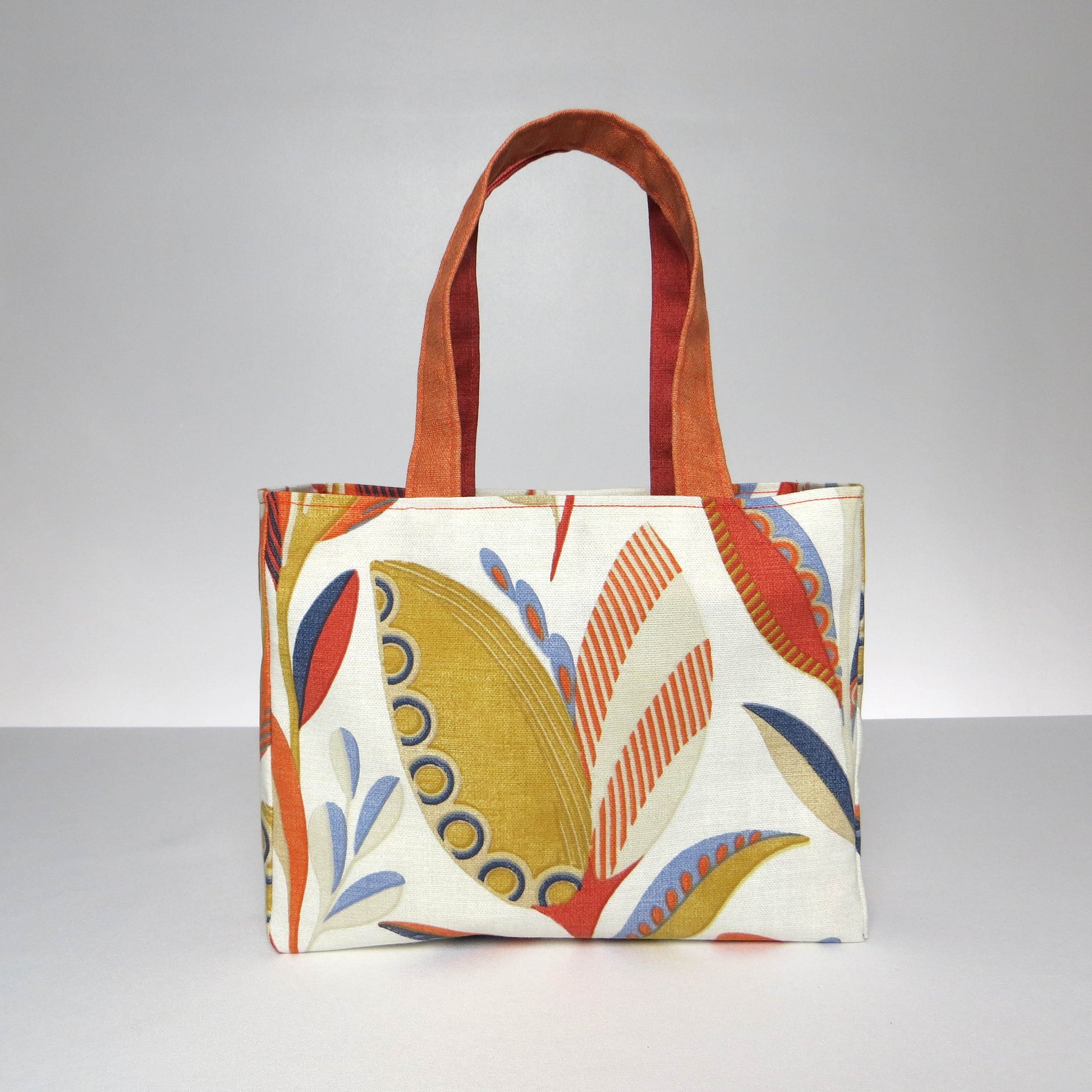 Small cotton tote bag with tulip pattern in shades of warm orange, rich ochre, and classic denim blue on an off-white background