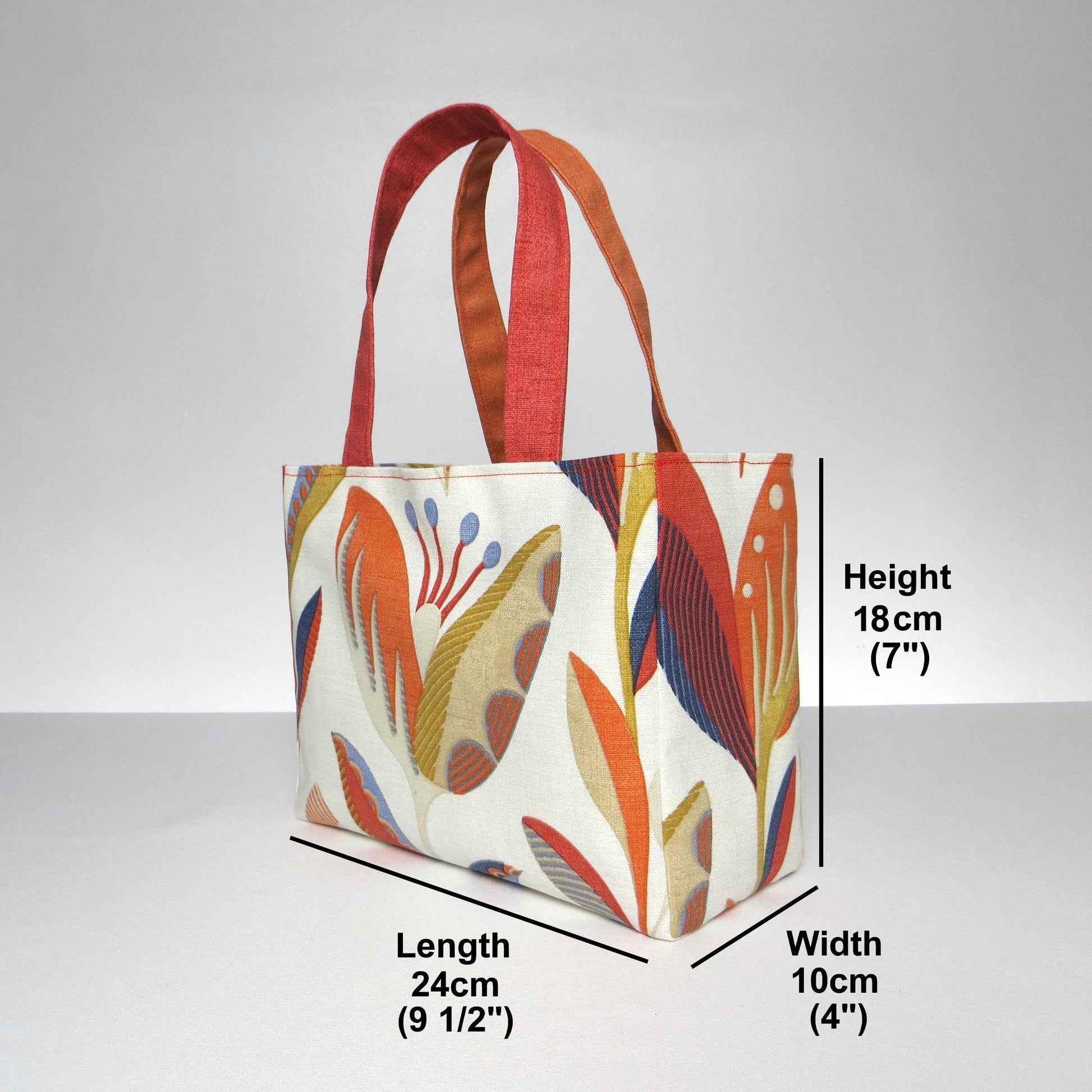 Small cotton tote bag with tulip pattern in shades of warm orange, rich ochre, and classic denim blue on an off-white background