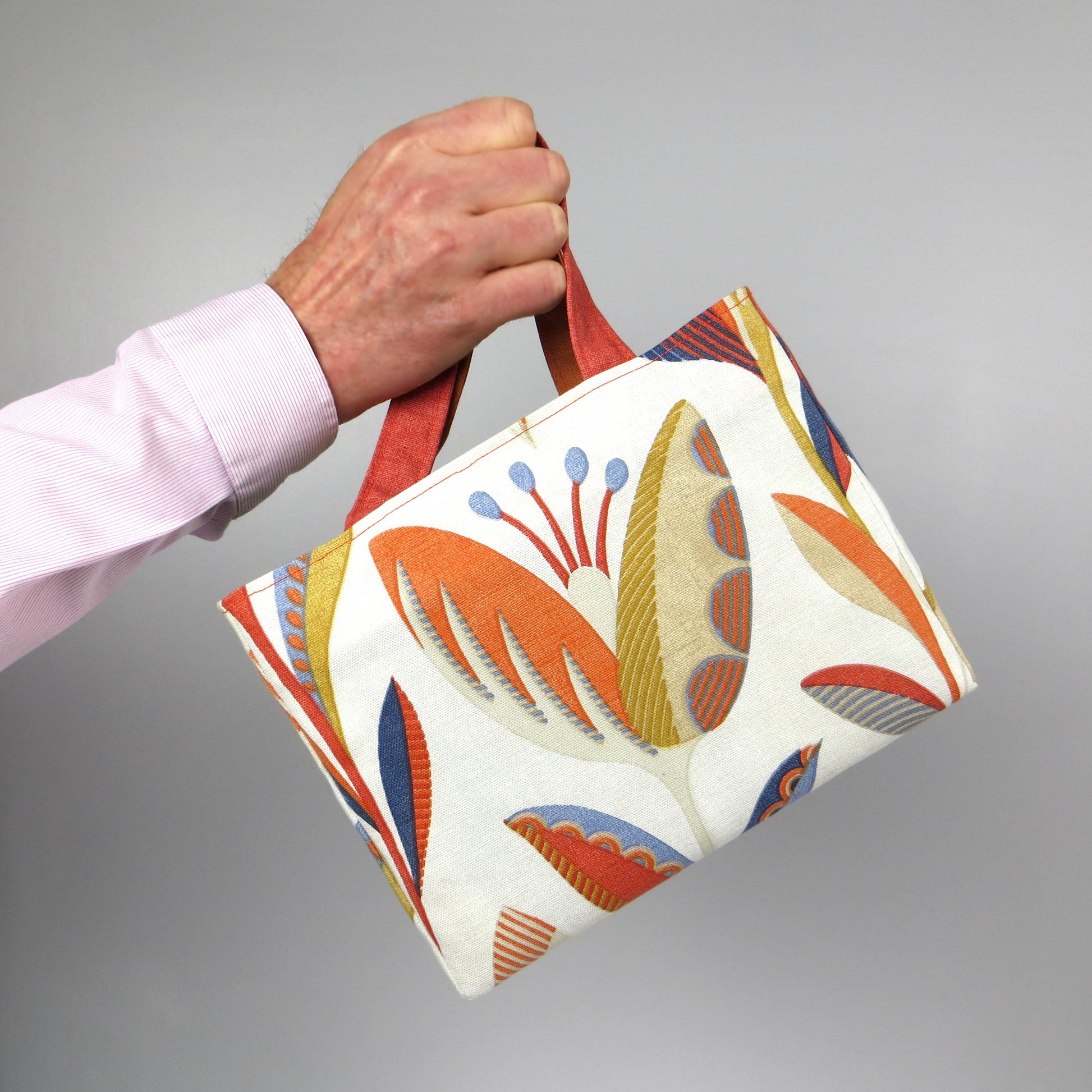 Small cotton tote bag with tulip pattern in shades of warm orange, rich ochre, and classic denim blue on an off-white background