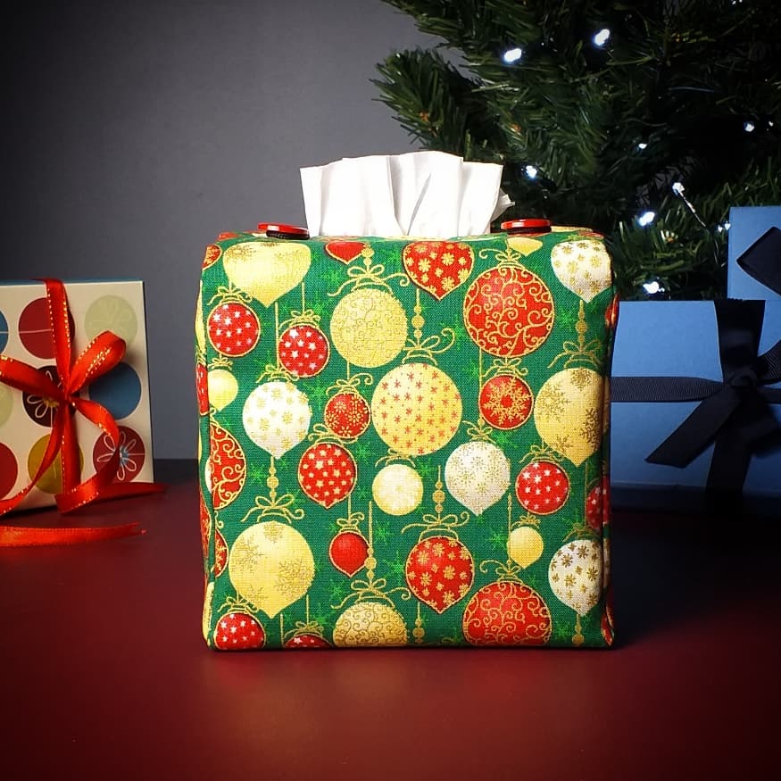 Square tissue box cover with holiday themed red, gold, and white Christmas baubles with metallic gold accent on green background